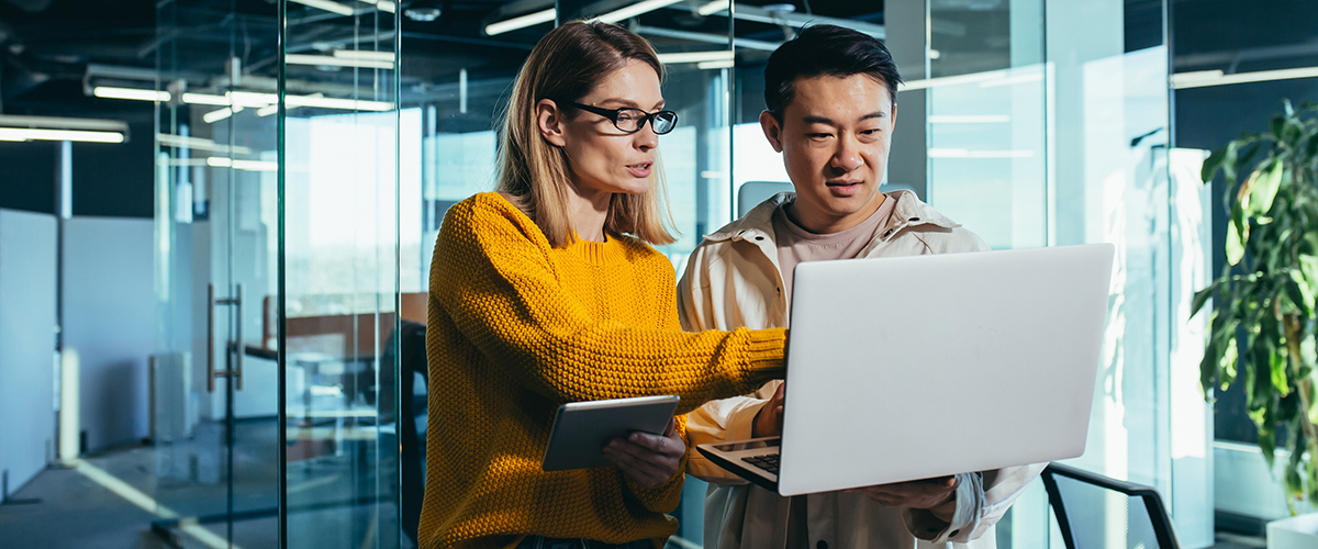 A man and a woman in an office looking at a laptop