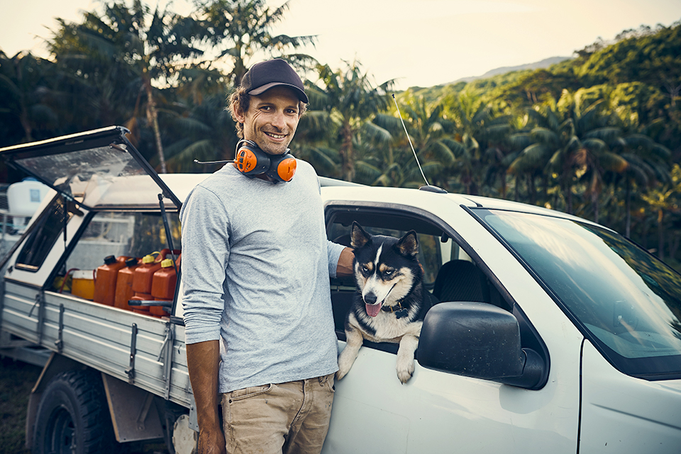 A tradie standing next to his ute with his arm around his dog
